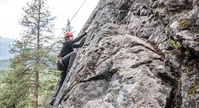 a student scales a rock wall on an outward bound trip for teens
